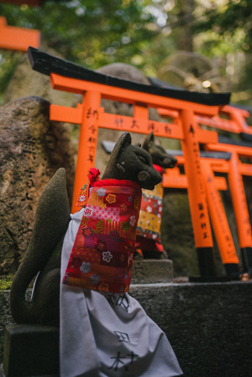 A stone fox statue wearing a red bib beside red torii gates at Fushimi Inari Shrine in Kyoto